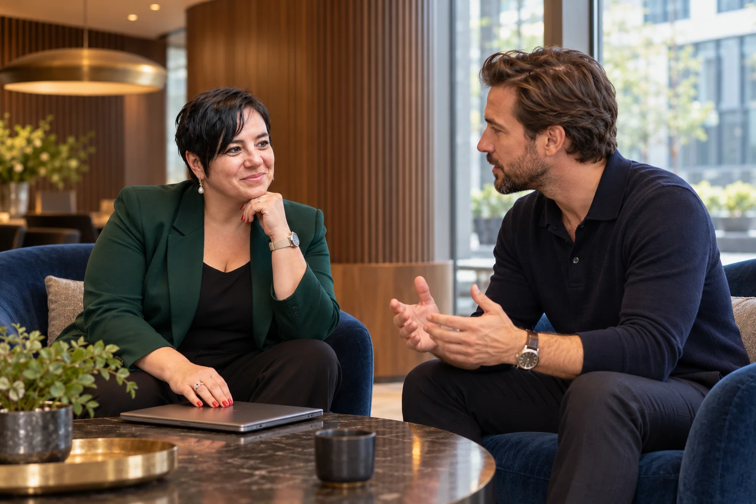 An Vermeulen luistert naar een ondernemer tijdens een gesprek in een modern kantoor.
