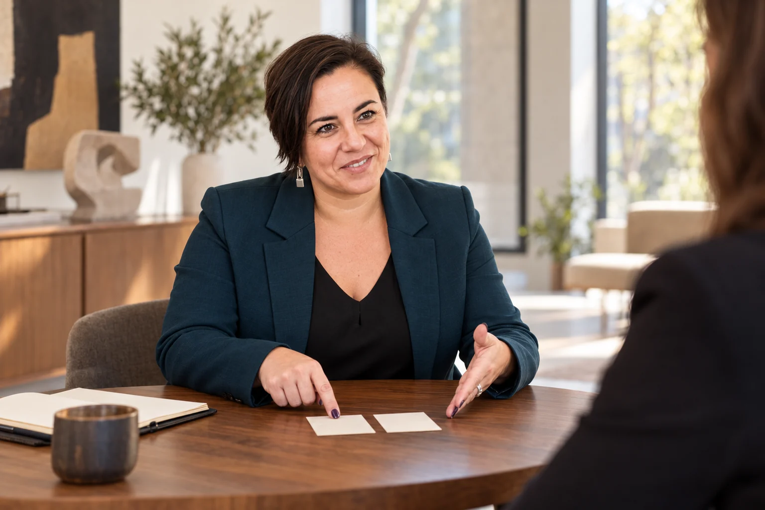 An Vermeulen in een petrolkleurige blazer bespreekt twee blanco kaarten aan een ronde tafel.