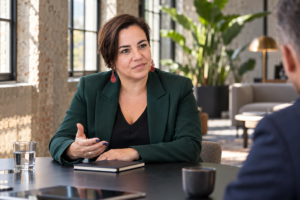 An Vermeulen in een groene blazer voert met een open handgebaar een gesprek in een industriële loft.