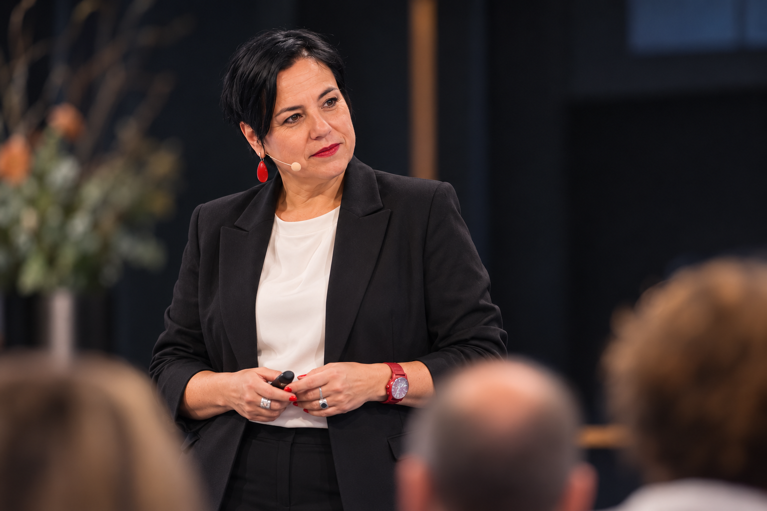 An Vermeulen in een zwarte blazer luistert op een podium naar een vraag uit het publiek.